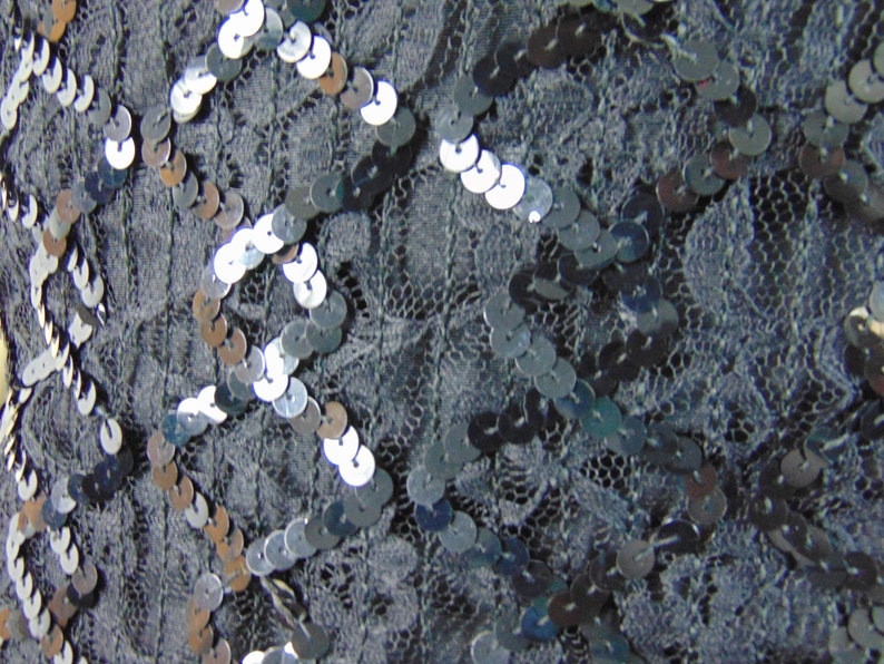 May include: Close-up of a black fabric with silver sequins arranged in a geometric pattern.