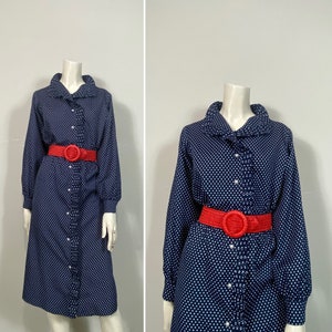 Pu&ograve; includere: Un abito a pois blu navy con colletto a volant e maniche lunghe. L'abito ha una chiusura con bottoni sul davanti e una cintura rossa.