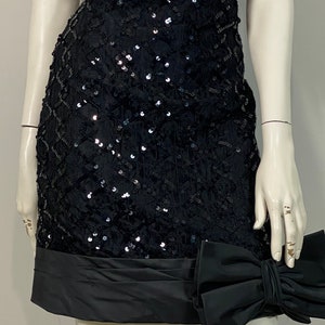 May include: A black sequined mini dress with a black satin bow at the hem.