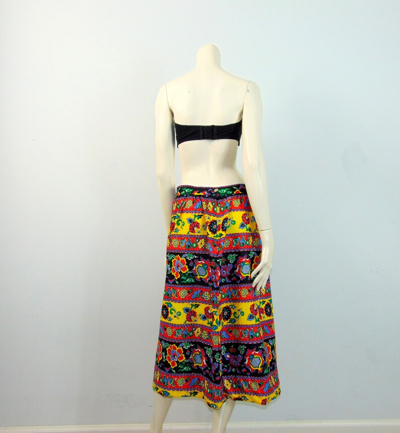 Puede incluir: Una falda larga amarilla con un estampado floral y geom&eacute;trico colorido. La falda tiene una cintura negra y una silueta recta, de l&iacute;nea A.