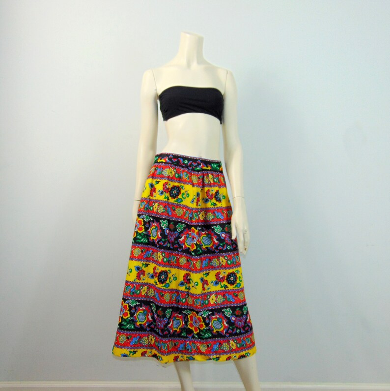 Puede incluir: Una falda midi colorida con fondo amarillo y estampado floral. La falda tiene una cintura ancha y una silueta fluida.