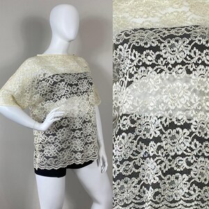 May include: A sheer ivory lace top with a wide, boat neckline and short sleeves. The lace has a floral pattern with a delicate, shimmery finish.