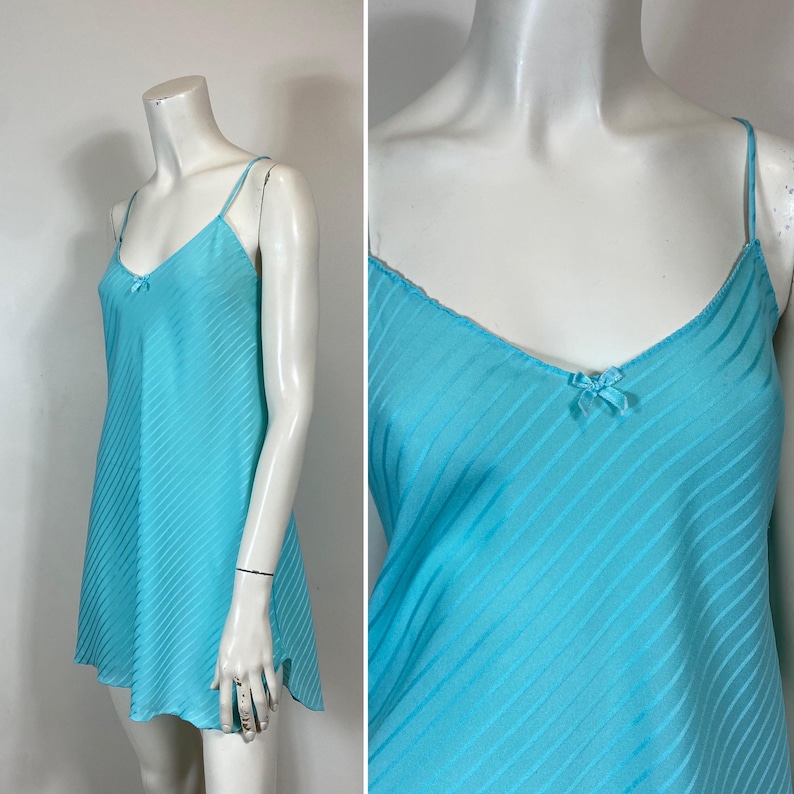 K&ouml;nnte beinhalten: Ein hellblaues Satin-Schlafkleid mit d&uuml;nnen Tr&auml;gern und einem Schleifendetail am Ausschnitt. Das Kleid hat ein gestreiftes Muster.