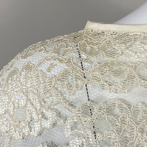 May include: Close-up of a white lace fabric with a delicate floral pattern. The fabric is soft and sheer, with a subtle shimmer.