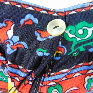 Puede incluir: Primer plano de una tela negra con un estampado floral colorido. La tela tiene una cremallera y un bot&oacute;n blanco.