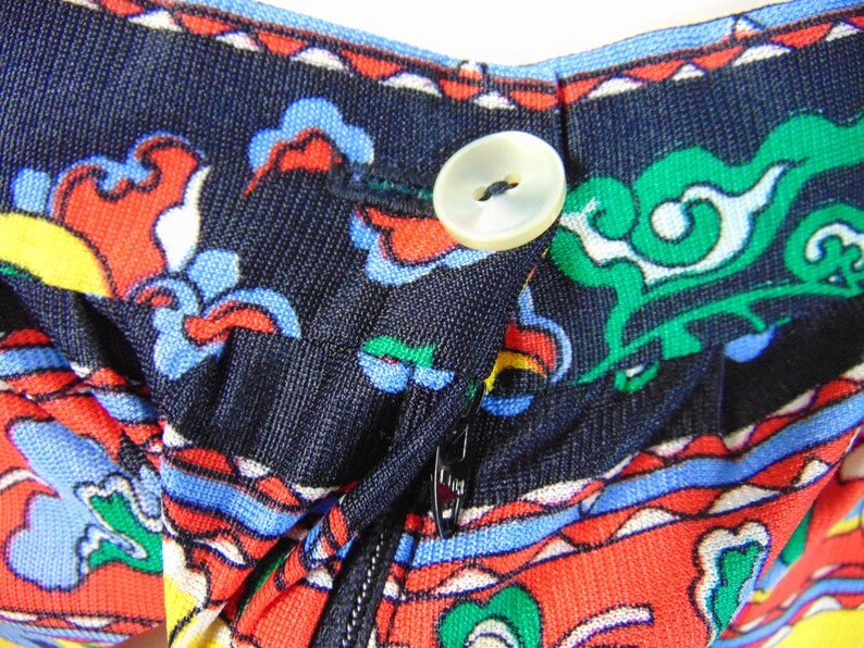 Puede incluir: Primer plano de una tela negra con un estampado floral colorido. La tela tiene una cremallera y un bot&oacute;n blanco.