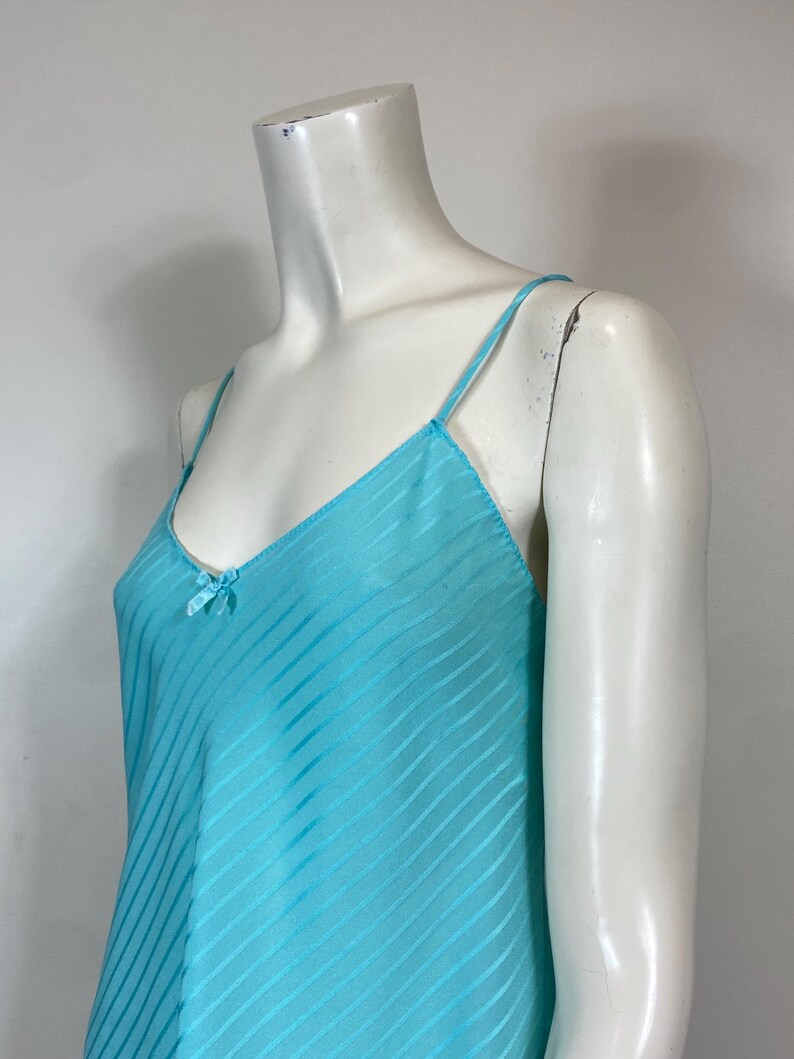 K&ouml;nnte beinhalten: Ein hellblaues, &auml;rmelloses, seidenes Schlupfkleid mit d&uuml;nnen Tr&auml;gern und einer Schleife am Ausschnitt.