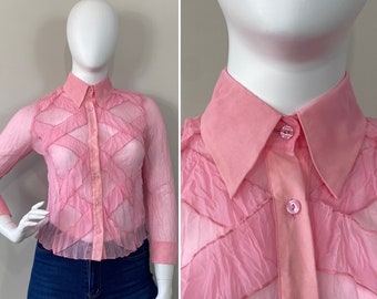 May include: A pink sheer button-up blouse with a ruffled design and a collar.