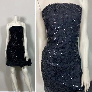 May include: A black strapless sequined mini dress with a black bow at the waist.