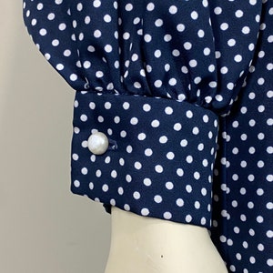 Pu&ograve; includere: Un abito blu navy con pois bianchi e un bottone di perla sul polsino.