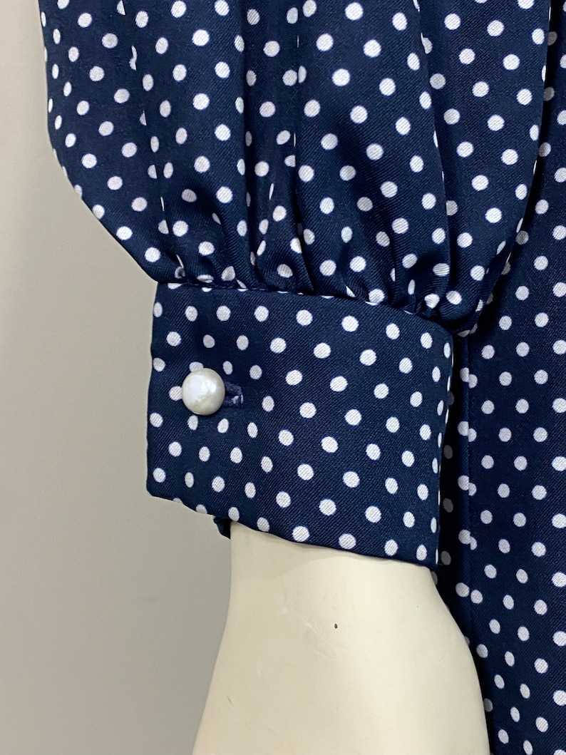 Pu&ograve; includere: Un abito blu navy con pois bianchi e un bottone di perla sul polsino.