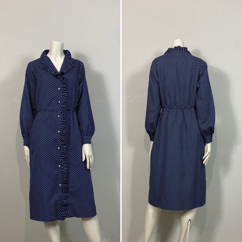 Pu&ograve; includere: Un abito blu navy con pois bianchi e un colletto a balze. L'abito ha maniche lunghe e una chiusura con bottoni sul davanti.