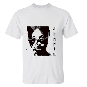 Puede incluir: Camiseta blanca con un gráfico en blanco y negro de una persona con gafas de sol, con el nombre "JENNIE" impreso verticalmente a la derecha. Un pequeño logotipo de Nike es visible a la izquierda.