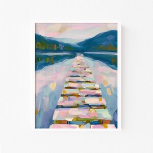 May include: An abstract painting of a pier extending into a lake, framed in white. The pier is composed of rectangular blocks in shades of pink, blue, and yellow. The water reflects the sky and distant mountains.
