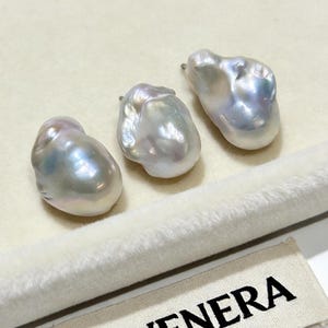 May include: Three irregular, lustrous baroque pearls with iridescent white and silver tones. Each pearl features a metallic post at the top for attachment. A small fabric tag with the black text SEVENERA is visible in the lower right corner.