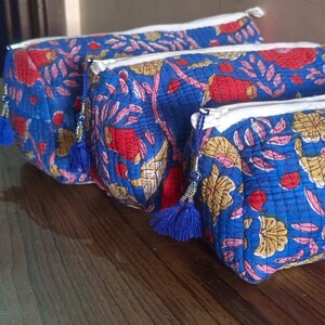 Puede incluir: Tres estuches acolchados con cremallera en tela azul vibrante con un patrón floral repetitivo en rojo y amarillo. Cada bolsa rectangular está terminada con un cierre de cremallera blanco y una pequeña borla azul en el tirador.