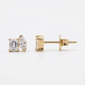May include: A pair of gold stud earrings, each featuring a clear emerald-cut gemstone positioned next to a clear marquise-cut gemstone. The earrings have a post back closure and are crafted from a polished yellow gold metal setting.