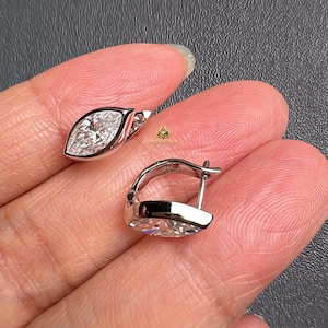 May include: A pair of marquise-cut diamond earrings. Each earring features a bezel-set, clear gemstone in a leaf shape. The earrings are set in a silver-coloured metal and have a hinged closure.
