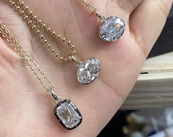 May include: Three diamond pendant necklaces with gold chains. The pendants feature oval and emerald-cut diamonds. The necklaces are displayed on a hand, showcasing the sparkle and clarity of the gemstones.
