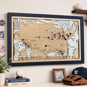 May include: A wooden baseball stadium map of the United States, with stadium locations marked by coloured pins. The map is framed in a dark blue frame and features baseball-themed cutouts. The words "BASEBALL STADIUM MAP" are at the bottom.