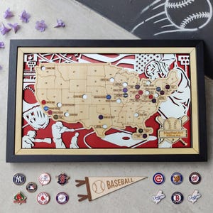 May include: A framed wooden map of the United States with baseball-themed cutouts and pin locations. The map is set against a red background and includes baseball pins and a pennant. The frame is black.