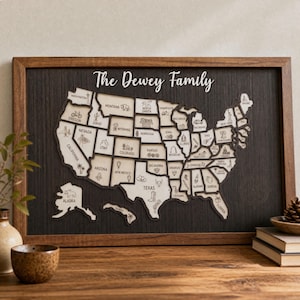 Puede incluir: Un cuadro decorativo de madera con un mapa de los Estados Unidos y el texto The Dewey Family en la parte superior. El mapa está compuesto por piezas de madera clara con iconos grabados, sobre un fondo con textura de madera oscura.