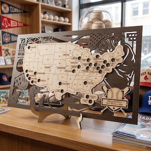 Peut inclure: Une carte en bois des stades de la MLB aux États-Unis, avec des balles de baseball marquant les emplacements. La carte est encadrée dans un cadre marron foncé et comprend un support. Le texte "MappaePilot MLB Stadium Map" est visible.