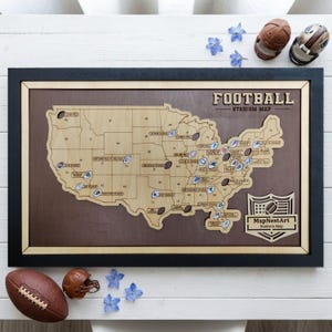 May include: A framed wooden map of the United States with football stadium icons. The map is in a black frame with a light brown border. The text "FOOTBALL STADIUM MAP" is at the top. A football and two miniature helmets are next to the map.