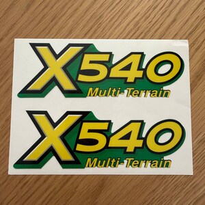 May include: Two rectangular adhesive decals featuring the text X540 in large yellow letters with a black outline, set against a green background. Below the X540, the words Multi-Terrain are printed in yellow with a black outline.