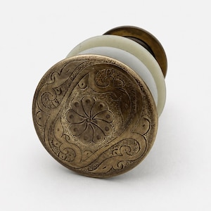 May include: A stack of antique brass cabinet knobs with a floral and scroll design. The knobs have a detailed, embossed pattern and a warm, aged finish. The stack includes a white and a light green knob.