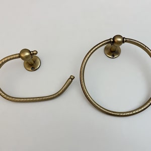 K&ouml;nnte beinhalten: Zwei antike Handtuchhalter aus Messing. Einer ist ein kreisf&ouml;rmiger Ring, der andere ein gebogener Stab. Beide haben ein strukturiertes, seilartiges Design und sind auf runden R&uuml;ckplatten montiert.
