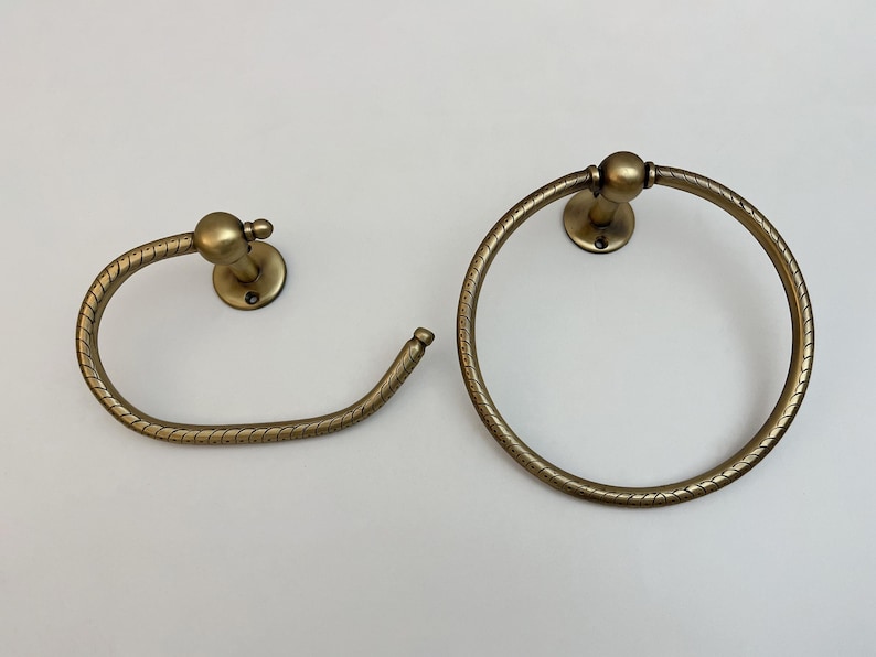 K&ouml;nnte beinhalten: Zwei antike Handtuchhalter aus Messing. Einer ist ein kreisf&ouml;rmiger Ring, der andere ein gebogener Stab. Beide haben ein strukturiertes, seilartiges Design und sind auf runden R&uuml;ckplatten montiert.