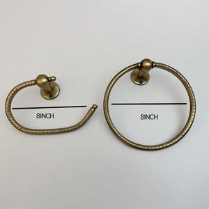 K&ouml;nnte beinhalten: Zwei antike Handtuchringe aus Messing. Einer ist ein kreisf&ouml;rmiger Ring, der andere ein gebogener Stab. Beide haben einen Durchmesser von 20 cm. Die Armaturen haben ein dekoratives, strukturiertes Design und sind auf runden Sockeln montiert.