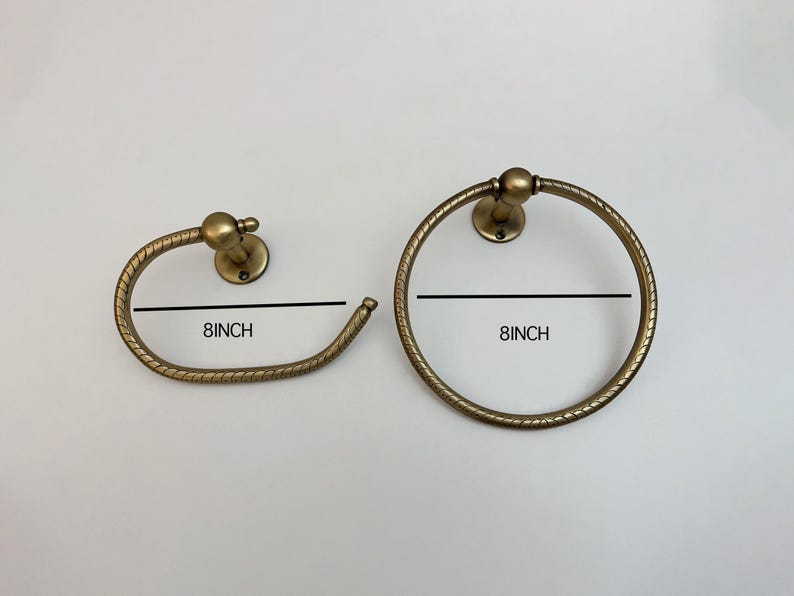K&ouml;nnte beinhalten: Zwei antike Handtuchringe aus Messing. Einer ist ein kreisf&ouml;rmiger Ring, der andere ein gebogener Stab. Beide haben einen Durchmesser von 20 cm. Die Armaturen haben ein dekoratives, strukturiertes Design und sind auf runden Sockeln montiert.