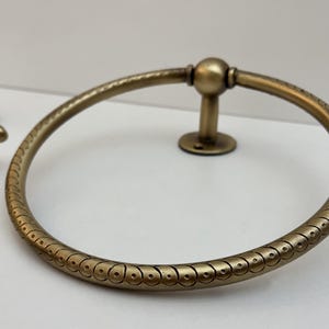 K&ouml;nnte beinhalten: Antiker Handtuchring aus Messing mit dekorativem Muster. Der kreisf&ouml;rmige Ring hat ein detailliertes Design und ist auf einer kleinen, runden Basis montiert. Zus&auml;tzliche passende Hardware ist sichtbar.