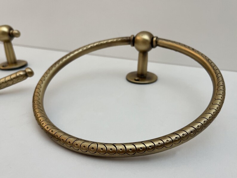 K&ouml;nnte beinhalten: Antiker Handtuchring aus Messing mit dekorativem Muster. Der kreisf&ouml;rmige Ring hat ein detailliertes Design und ist auf einer kleinen, runden Basis montiert. Zus&auml;tzliche passende Hardware ist sichtbar.