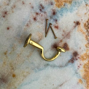 Pu&ograve; includere: Un gancio in metallo color oro con un design curvo e due viti. Il gancio ha una base circolare e un'estremit&agrave; arrotondata. Le viti sono color bronzo e hanno una punta.