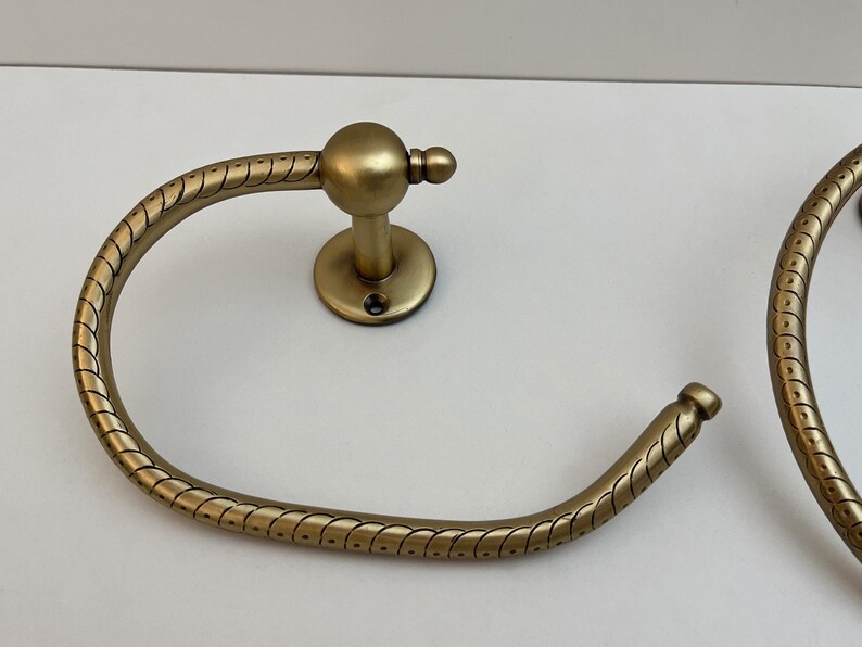 K&ouml;nnte beinhalten: Zwei antike Handtuchringe aus Messing. Jeder Ring hat ein kreisf&ouml;rmiges Design mit einer seilartigen Textur. Die Ringe sind auf einer runden Basis mit einem zentralen Pfosten und einer dekorativen Kugel befestigt. Badezimmerdekoration.