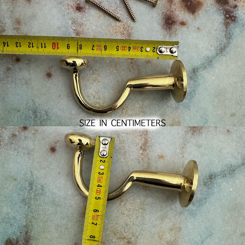 Pu&ograve; includere: Un gancio in metallo dorato con base rotonda e braccio curvo, lungo circa 7 cm. Il testo "SIZE IN CENTIMETERS" &egrave; visibile. Sono presenti anche diverse viti.