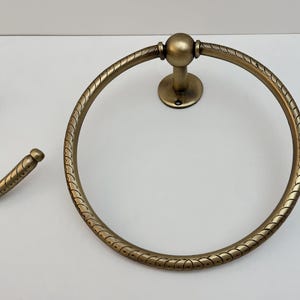 K&ouml;nnte beinhalten: Antiker Handtuchring und passender Haken in Messingoptik. Der kreisf&ouml;rmige Handtuchring hat ein dekoratives, seilartiges Muster am Rand. Der Haken hat ein &auml;hnliches Design. Badezimmer-Hardware.