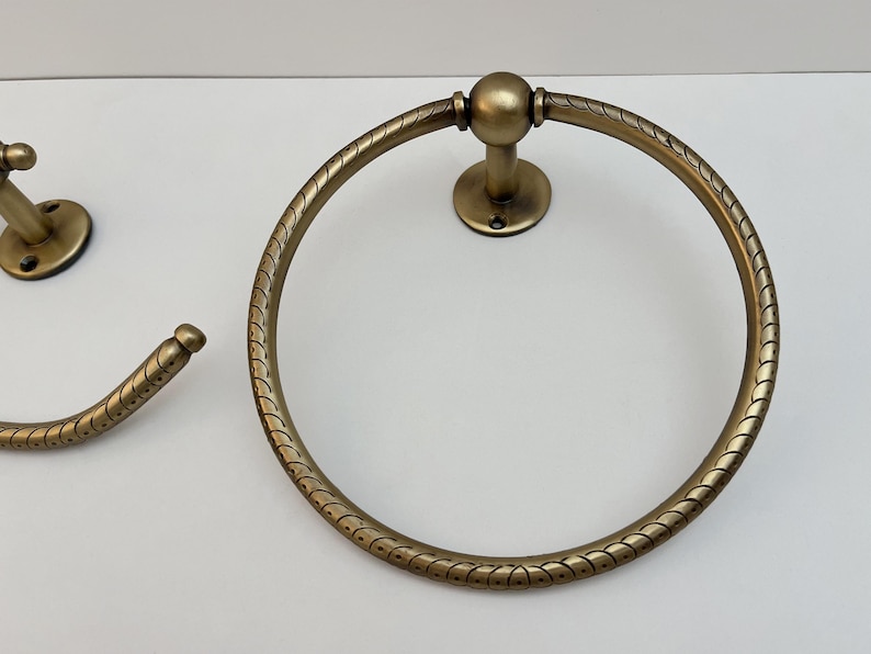 K&ouml;nnte beinhalten: Antiker Handtuchring und passender Haken in Messingoptik. Der kreisf&ouml;rmige Handtuchring hat ein dekoratives, seilartiges Muster am Rand. Der Haken hat ein &auml;hnliches Design. Badezimmer-Hardware.