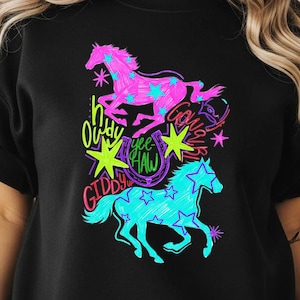May include: Black sweatshirt featuring a neon graphic of two horses with star patterns. The design includes the phrases "Howdy", "Giddy Up", and "Yee Haw". The horses are pink and turquoise, with yellow and green accents.