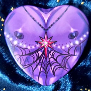 May include: A purple heart-shaped resin charm with a black spiderweb design and a red star pendant with a white chain.