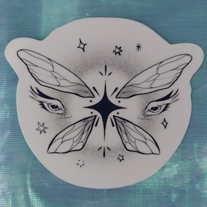 Könnte beinhalten: Ein weißer Aufkleber mit einer schwarz-weißen Illustration eines Schmetterlings mit Augen und einem Stern in der Mitte. Der Schmetterling hat Flügel mit einem detaillierten Adernmuster. Um den Schmetterling herum befinden sich kleine Sterne.