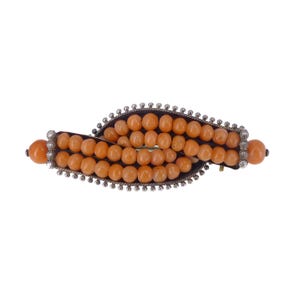 May include: A silver and coral brooch with a twisted design. The brooch is made of small, round coral beads set in a silver frame.