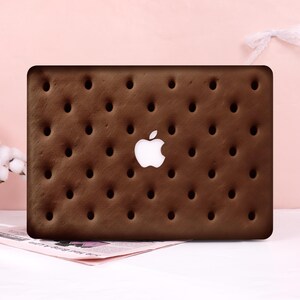May include: A rectangular laptop skin featuring a dark brown, textured chocolate wafer pattern with a grid of small, circular indentations. The design includes a central cutout that reveals the white Apple logo on the laptop surface.