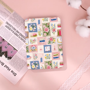 Könnte beinhalten: Eine rechteckige E-Reader-Hülle mit einem sich wiederholenden Muster aus briefmarkenartigen Quadraten. Jedes Quadrat zeigt Illustrationen von bunten Blumen, Bücherstapeln, offenen Büchern, brennenden Kerzen und Teetassen in Rosa, Blau und Grün.
