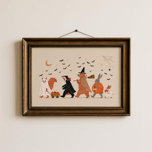 May include: A framed horizontal print featuring a whimsical illustration of five woodland animals in Halloween costumes. A squirrel, badger, bear, rabbit, and mouse walk together under a crescent moon and black bats on a light beige background.