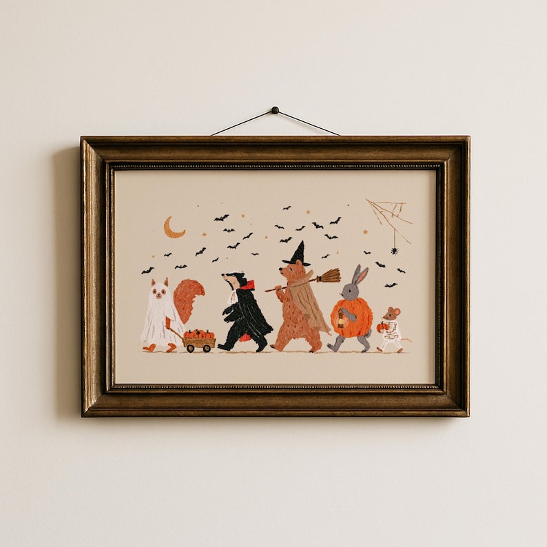 May include: A framed horizontal print featuring a whimsical illustration of five woodland animals in Halloween costumes. A squirrel, badger, bear, rabbit, and mouse walk together under a crescent moon and black bats on a light beige background.
