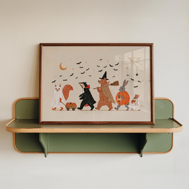 May include: A framed horizontal art print featuring a whimsical Halloween scene with a squirrel in a ghost costume, a badger in a cape, a bear in a witch hat, a rabbit in a pumpkin suit, and a mouse in a skeleton costume, all under black bats.